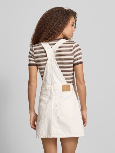 Frauenmodel trägt Leicht ausgestelltes Jeanskleid aus reiner Baumwolle von Tommy Jeans in heller Denim-Optik mit Brusttasche, Mini-Länge, Label-Stitching-Applikation und Latzträgern, Ganzkörperansicht Rückansicht.