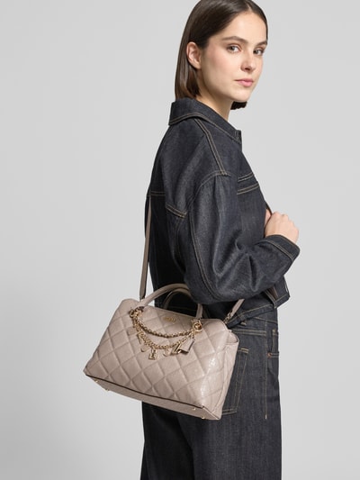 Frauenmodel trägt Handtasche in Leder-Optik Modell 'Libby' von Guess in Stepp-Optik mit Logo-Detail und Zierbesatz, Ganzkörperansicht von vorne.