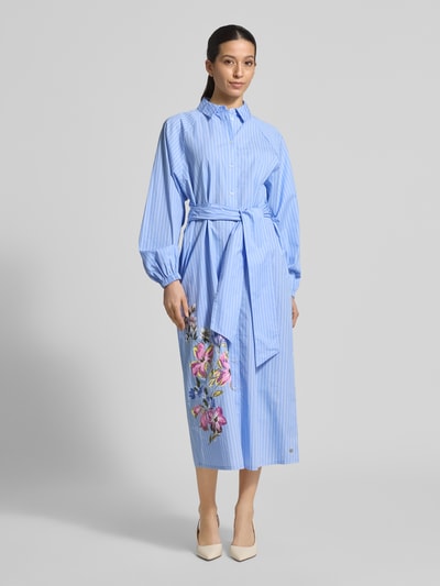 Vrouwenmodel draagt Regular Fit maxi-jurk met bloemenprint van Fynch-Hatton van puur katoen, met lange mouwen en overhemdkraag, lichtblauw met kleurrijke bloemen, knoopsluiting, getailleerd met afneembaar stoffen band, vooraanzicht in volle lengte.