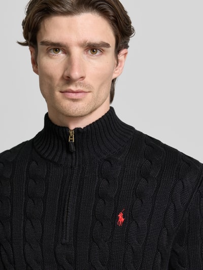 Męski model nosi Regular Fit Troyer aus reiner Baumwolle od Polo Ralph Lauren, czarny sweter z warkoczowym wzorem, detal logo, dzianina, krótki zamek, długi rękaw, wykończenia prążkowane, widok z przodu, zbliżenie na górną część ciała.