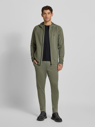 Männermodel draagt Regular Fit Sweatpants uit snel drogend materiaal Model 'HICON ACTIVE' van BOSS Green, look: effen, labelprint, elastische boord, flatlock-internaden, zij-steekzakken, achterzak, kleur: olijfgroen, full-body vooraanzicht.