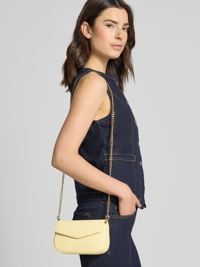 Frauenmodel trägt Crossbody Bag mit Innenfach Modell 'VANJA' von Seidenfelt in Creme mit Überschlag, Magnetverschluss, Gliederketten-Schulterriemen, Ganzkörperansicht von vorne.