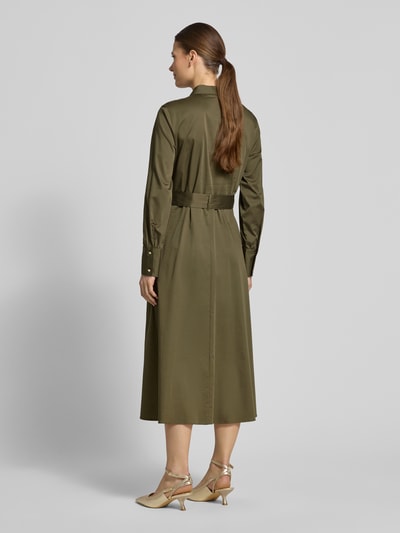 Vrouwenmodel draagt Regular Fit Midikleid mit Umlegekragen van comma, elastische katoenmix in olijfgroen, afneembare stoffen riem, lange mouwen, knoopsluiting, getailleerde regular fit, ruglengte 120 cm, borstwijdte 45 cm, mouwlengte 62 cm. Volledige lichaamsweergave achteraan.