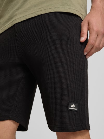 Männermodel trägt Shorts mit Strukturmuster und Label-Detail von Alpha Industries in Schwarz, Regular-Fit, Nahaufnahme Oberschenkel.