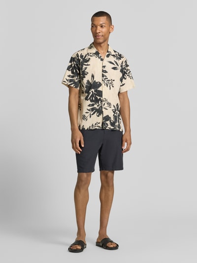 Männermodel trägt Relaxed Fit Freizeithemd mit Reverskragen Modell 'BLAVENICE' von Jack & Jones Premium, beige mit schwarzem Blumenmuster, Bio-Baumwoll-Mix, Knopfleiste, Ganzkörperansicht von vorne.