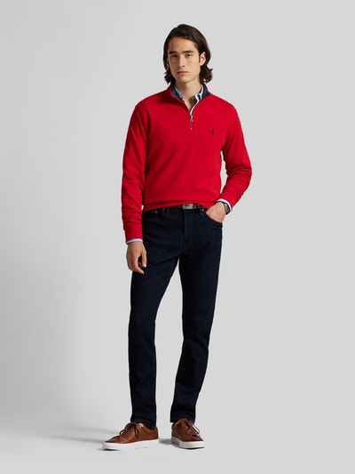 Männermodel trägt Regular Fit Sweatshirt aus Baumwoll-Mix von Polo Ralph Lauren in Rot mit blauen Jeans, Ganzkörperansicht von vorne.