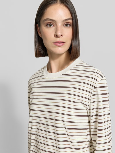 Frauenmodel trägt cremeweißes, braun gestreiftes Boxy Fit Langarmshirt aus reiner Baumwolle Modell 'ESSENTIAL' von Selected, Damen Langarmshirt, Nahaufnahme Oberkörper.