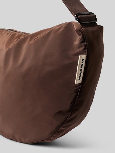 Produktfoto, Bauchtasche mit Logo-Detail von AY STUDIOS in Braun, glatte Oberfläche, verstellbarer Schulterriemen, Reißverschluss, Detailaufnahme.