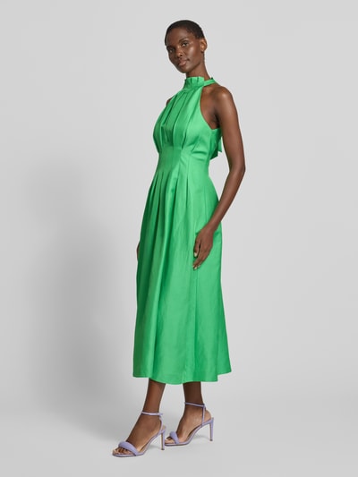 Frauenmodel trägt Cocktailkleid mit Drapierungen Modell 'Miller' von Forever New aus Viskose-Leinen-Mix, A-Linie, Midikleid, strahlendes Grün, Neckholder, rückseitige Schnürung, glatte Textur, Ganzkörperansicht von vorne.