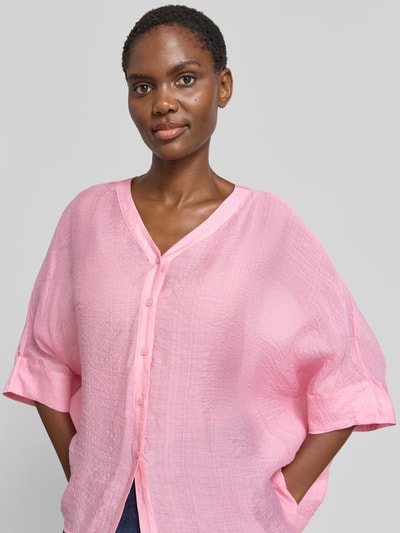 Frauenmodel trägt Relaxed Fit Bluse aus Viskose-Mix mit 3/4-Arm von Comma in Rosa, V-Ausschnitt, Knopfleiste, Nahaufnahme Oberkörper. Rückenlänge bei Größe S 62 cm, Ärmellänge S 18 cm. Textur leicht strukturiert.
