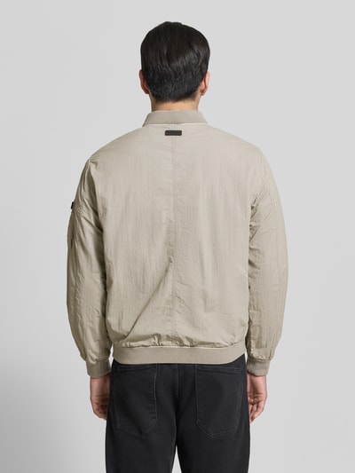 Männermodel trägt Blouson mit Label-Patches Modell 'IBE' von khujo in Beige mit Reißverschluss, Stehkragen, Gerader-Schnitt, Ganzkörperansicht Rückansicht.