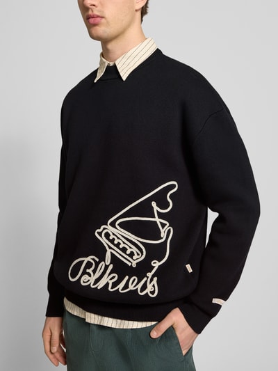 Männermodel trägt Strickpullover mit Label-Detail von BLKVIS, reine Baumwolle, lockerer Schnitt, gerippte Abschlüsse, Nahaufnahme Oberkörper.