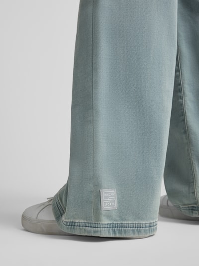 Frauenmodel trägt Wide Fit Jeans aus Baumwoll-Mix von Marc Cain in Hellblau mit sichtbarem Label, strukturierte Oberfläche, Nahaufnahme Bein. Damen Jeans von Marc Cain, elastischer Baumwoll-Mix, Wide Fit, elastischer Bund mit Tunnelzug, Eingrifftaschen, Bundweite bei Größe 36: 40 cm, Innenbeinlänge bei Größe 36: 83 cm.