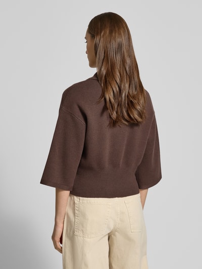 Frauenmodel trägt Strickjacke aus Viskose-Mix Modell 'SHYLA' von Noisy May in Braun mit lockerer Passform, 3/4-Arm, gerippte Abschlüsse, Umlegekragen, durchgehende Knopfleiste, Rückenlänge 48 cm, Ärmellänge 31 cm, Ganzkörperansicht Rückansicht.