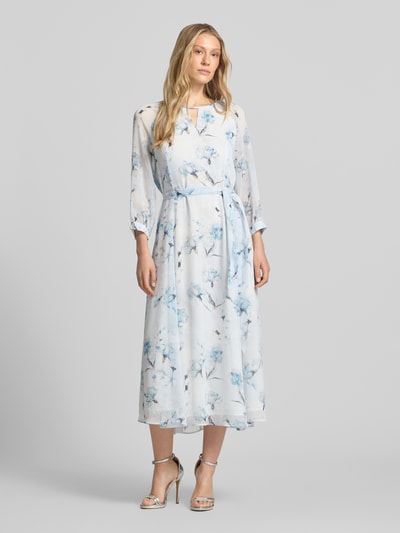 Frauenmodel trägt Midikleid mit Bindegürtel von More & More mit blauem Blumenmuster, Taillierter Schnitt, Rundhalsausschnitt mit Cut-Out, 3/4-Arm, Rückseitiger Schlüsselloch-Ausschnitt und Reißverschluss, Rückenlänge 128 cm, Brustweite 42 cm, Ärmellänge 58 cm, fließende Textur, Ganzkörperansicht von vorne.