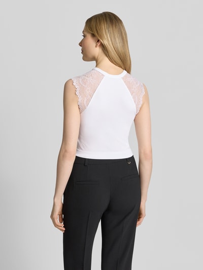 Männermodel trägt Crop Top mit Spitzenbesatz Modell 'MILLIE' von Guess, biały materiał z elastycznym dodatkiem, krój slim fit, długość z tyłu 37 cm, widok całej sylwetki z tyłu