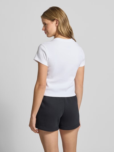 Frauenmodel trägt Cropped T-Shirt in Ripp-Optik mit Logo von Nike aus Baumwoll-Elasthan-Mix, weiß, Schwarze Shorts, Rückenlänge 48 cm, Ganzkörperansicht Rückansicht.