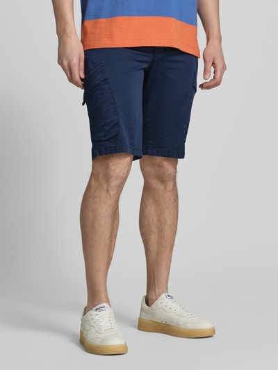 Männermodel trägt Regular Fit Cargoshorts aus Baumwoll-Mix von Brax in Dunkelblau mit seitlichen Eingrifftaschen und Cargotaschen, Nahaufnahme Oberkörper bis Knie, unifarbene Optik