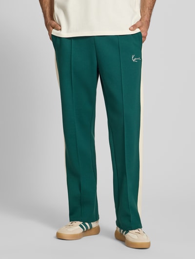 Männermodel trägt Straight Fit Sweatpants mit Logo-Stitching van KARL KANI in groen met beige, elastische materiaalmix met katoen, straight fit, gestikt logo, elastische band, binnenbeenlengte maat M 78 cm, ganzkörperansicht van voren.