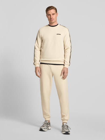 Männermodel trägt Sweatshirt mit Label-Details und Rundhalsausschnitt von EA7 Emporio Armani in Creme, Baumwoll-Mix, Regular-Fit, Ganzkörperansicht von vorne. Rückenlänge bei Größe M: 63 cm, Ärmellänge bei Größe M: 66 cm.