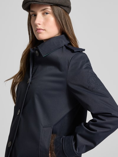 Frauenmodel trägt Regular Fit Trenchcoat mit Umlegekragen von Lauren Ralph Lauren in Dunkelblau, Logo-Detail am Ärmel, Nahaufnahme Oberkörper.