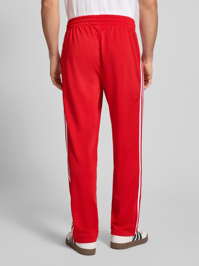 Männermodel trägt Spodnie dresowe z elastycznym pasem od adidas Originals, luźny krój, wyhaftowane logo, kieszenie zapinane na zamek błyskawiczny, długość wewnętrzna nogawki w rozmiarze M 79 cm, widok całej sylwetki z tyłu.