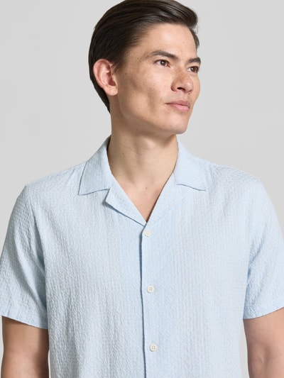 Męski model nosi Relaxed Fit Freizeithemd mit Leinen-Anteil od Lindbergh, jasnoniebieski, krótki rękaw, kołnierz rewersowy, guzik, teksturowany wzór, mieszanka bawełny z lnem, długość tyłu w rozmiarze M 73 cm, szerokość w rozmiarze M 46 cm, długość rękawa w rozmiarze M 26 cm, zbliżenie na górną część ciała.
