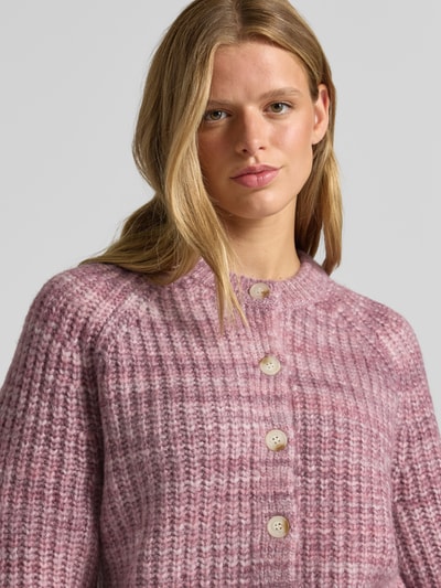 Frauenmodel trägt Cardigan mit Woll-Anteil und Rundhalsausschnitt von REVIEW, grobe Struktur, Knopfleiste, rosa-lila Töne, Nahaufnahme Oberkörper. Material-Mix mit Woll-Anteil, gerader Schnitt, Rückenlänge 52 cm, Ärmellänge 67 cm.
