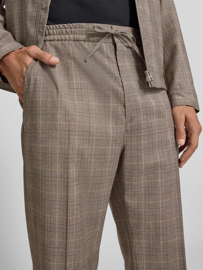 Männermodel trägt Straight Fit Stoffhose mit Bügelfalten Modell 'Cove' von Tiger Of Sweden aus bawełna, kanty, wpuszczane kieszenie, kieszeń z tyłu, pas z tunelem, szerokość w rozmiarze 50: 39 cm, długość wewnętrzna nogawki 80 cm, jasnobrązowe krata, tekstura gładka, detalowanie szwów, zbliżenie na pas i kieszeń, nahaufnahme górnej części ciała.