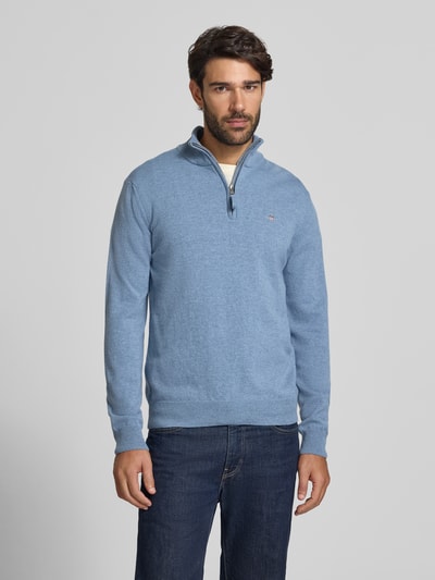 Männermodel trägt Pullover aus reiner Wolle von GANT in Hellblau, Feinstrick, hochgeschlossener Troyerkragen, Reißverschluss, Langarm, Ganzkörperansicht von vorne