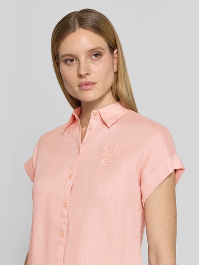Frauenmodel trägt Relaxed Fit Hemdbluse aus reinem Leinen von Lauren Ralph Lauren, Farbe Hellrosa, Optik: Unifarben, Materialverarbeitung: Flammgarn, kurzarm, Logo-Stitching, Hemdkragen, Knopfleiste, Nahaufnahme Oberkörper.