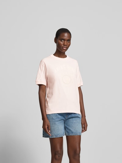 Frauenmodel trägt Regular Fit T-Shirt mit Logo-Print von Anine Bing aus reiner Baumwolle, Rundhalsausschnitt, kurzärmelig, Farbe Rosa, kombiniert mit Jeansshorts, Ganzkörperansicht von vorne.