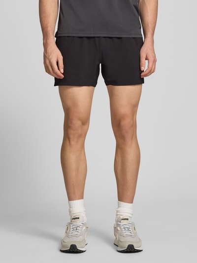 Männermodel trägt Regular Fit Shorts mit Logo-Print von PUMA PERFORMANCE in Schwarz, elastischer Bund, Eingrifftaschen, Ganzkörperansicht von vorne.