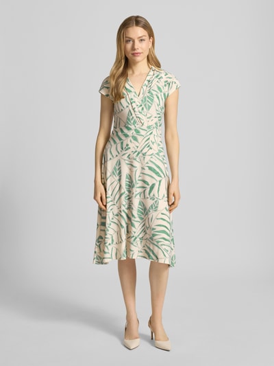 Modelka kobieca nosi Midikleid in Wickel-Optik mit V-Ausschnitt Modell 'Ca44rrara' od ZABAIONE, beżowo-zielony print liści, materiał elastyczny, krój slim fit, szerokość w rozmiarze S: 45 cm, długość tyłu: 105 cm, widok całej sylwetki z przodu.