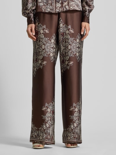 Kobiece modelka nosi Stoffhose mit elastischem Bund od Neo Noir, brązowy materiał, luźny krój, wzór paisley, zbliżenie na nogi, przód.