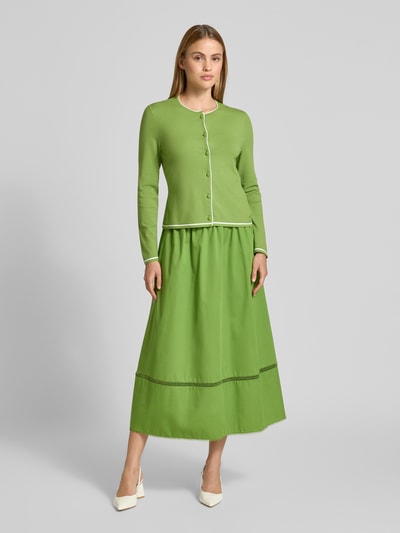 Frauenmodel trägt Cardigan aus Viskose-Mix mit Kontrastkante von Marc Cain in Grün, Gerader-Schnitt, Rundhalsausschnitt, Knopfleiste, Rückenlänge 51 cm, Ärmellänge 59 cm, Ganzkörperansicht von vorne.