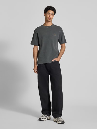 Männermodel trägt T-Shirt mit Strukturmuster Modell 'Nelson' von Carhartt Work In Progress in Dunkelgrau, Relaxed Fit, Ganzkörperansicht von vorne.