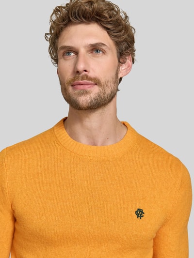 Männermodel trägt Slim Fit Strickpullover aus reiner Wolle mit Label-Stitching von MCNEAL in Gelb, Nahaufnahme Oberkörper, reine Wolle, gerippte Abschlüsse, KI-modifiziertes Bild.