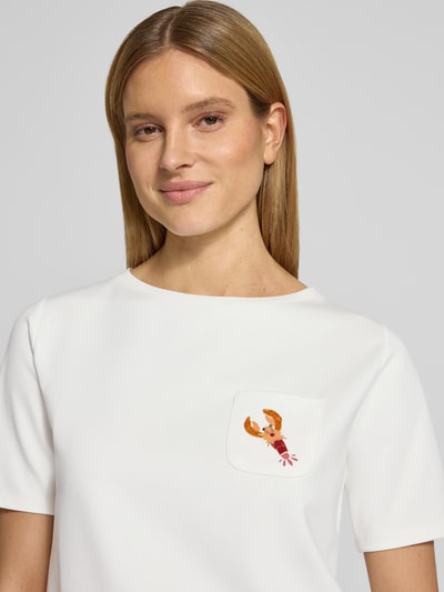 Frauenmodel trägt T-Shirt mit Brusttasche und Motiv von More & More, Viskose-Mix mit Stretch-Anteil, Perlen, Rundhalsausschnitt, Nahaufnahme Oberkörper.