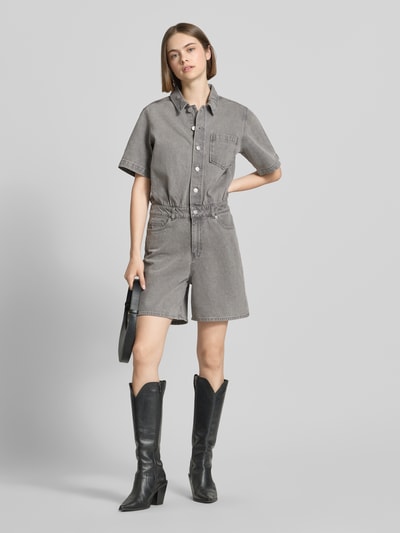 Frauenmodel trägt Regular-Fit Playsuit in Denim-Optik Modell 'Fillipa' von JJXX, Reine Baumwolle, Knopfleiste, Kurzärmelig, 5-Pocket-Design, Umlegekragen, Brusttasche, graue Farbtöne, mittlere Beinlänge, strukturierte Textur, Ganzkörperansicht von vorne.