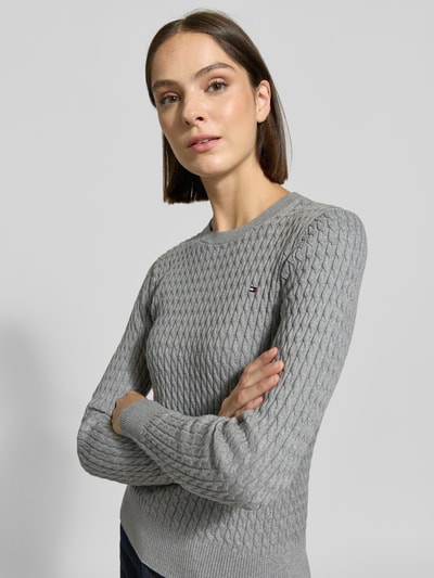 Frauenmodel trägt Regular Fit Pullover aus reiner Baumwolle von Tommy Hilfiger in hellgrau mit strukturierter Zopfstrickoptik, Nahaufnahme Oberkörper, Damen Pullover von Tommy Hilfiger.