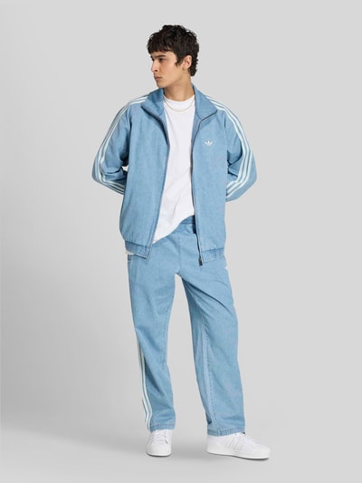 Männermodel trägt Relaxed Fit Trainingshose aus Baumwoll-Mix von adidas Originals in Denim-Optik mit Logo-Applikation, Ganzkörperansicht von vorne.