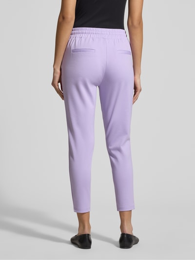 Modelka nosi Slim Fit Stoffhose mit Viskose-Anteil Modell 'Kate' von ICHI, kolor liliowy, materiał elastyczny, krój slim fit, szerokość w rozmiarze S: 38 cm, długość nogawki: 65 cm, widok całej sylwetki z tyłu.
