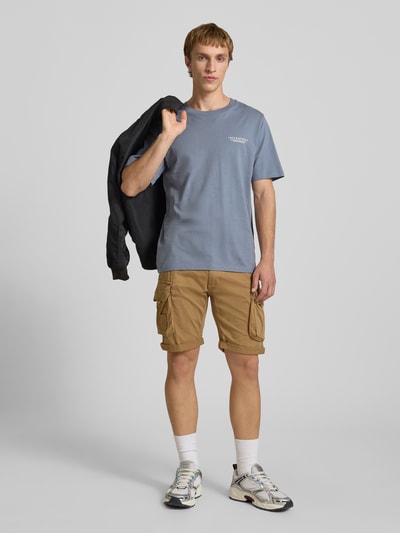 Männermodel trägt Herren T-Shirt mit Label-Print und Rundhalsausschnitt von Jack & Jones aus Reine Baumwolle, Regular-Fit, Rückenlänge 70 cm, sandfarbene Shorts, Ganzkörperansicht von vorne.