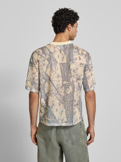 Männermodel trägt T-Shirt aus Mesh mit Logo von KARL KANI, beige-graues Muster, Regular Fit, Rundhalsausschnitt, Ganzkörperansicht Rückansicht.