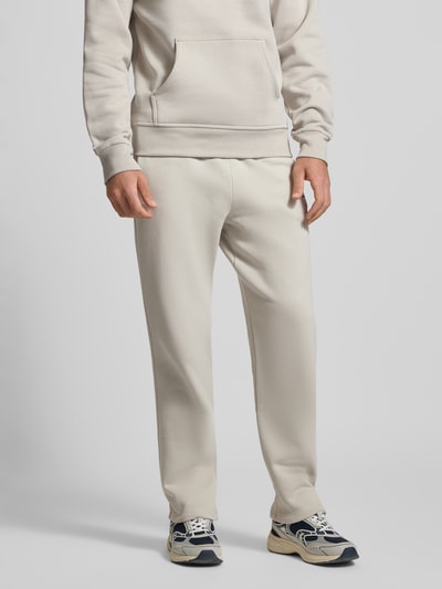 Męski model nosi Straight Fit Sweatpants mit Label-Stitching od CHAMPION z mieszanki bawełny, elastyczny pas, jasny kolor, Ganzkörperansicht von vorne. Długość wewnętrzna nogawki w rozmiarze M: 70 cm.