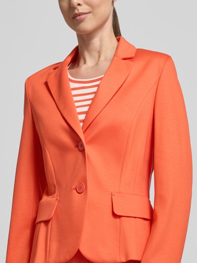 Frauenmodel trägt Slim Fit Blazer aus Viskose-Mix von Marc Cain in leuchtendem Orange mit Reverskragen, Pattentaschen, 2-Knopfleiste, Nahaufnahme Oberkörper. Rückenlänge bei Größe 36: 55 cm, Brustweite 41 cm, Ärmellänge 62 cm.