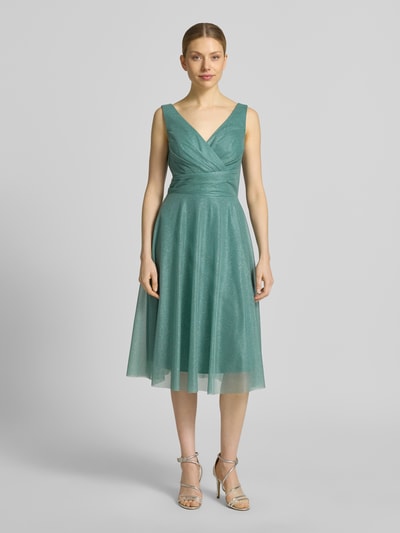Frauenmodel trägt Knielanges Cocktailkleid mit V-Ausschnitt von TROYDEN COLLECTION aus Chiffon, taillierter Schnitt, Knielänge, breite Träger, Rückenreißverschluss, petrolfarbener Stoff, feine Textur, Ganzkörperansicht von vorne.