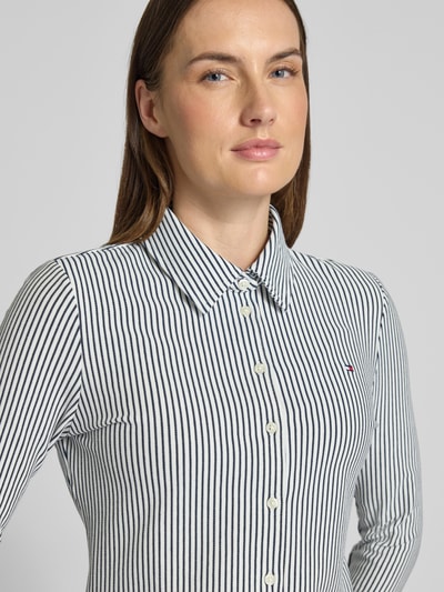 Vrouwenmodel draagt Slim Fit Hemdbluse aus Baumwoll-Mix van Tommy Hilfiger met allover-streep, logo-stiksel, katoenmengsel, close-up bovenlichaam.