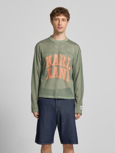 Männermodel trägt Longsleeve mit Label-Patch und Rundhalsausschnitt von KARL KANI, Boxy-Fit, Logo-Print, grün, Rückenlänge 63 cm, Ganzkörperansicht von vorne.